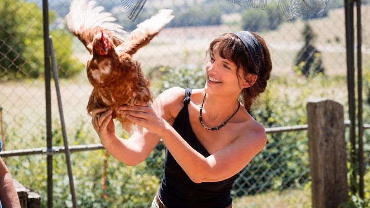Ariane, hilare, tenant une poule à bout de bras